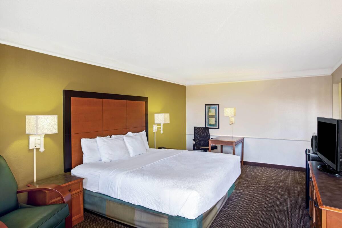 A hotel room with a bed, a desk, a chair, a television, and a lamp.