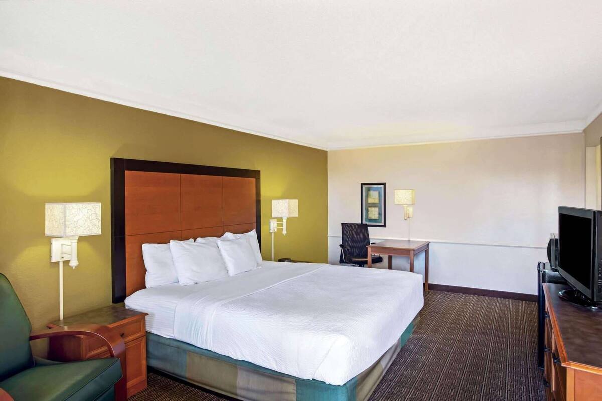 A hotel room with a bed, a desk, a chair, a television, and two wall-mounted lamps.