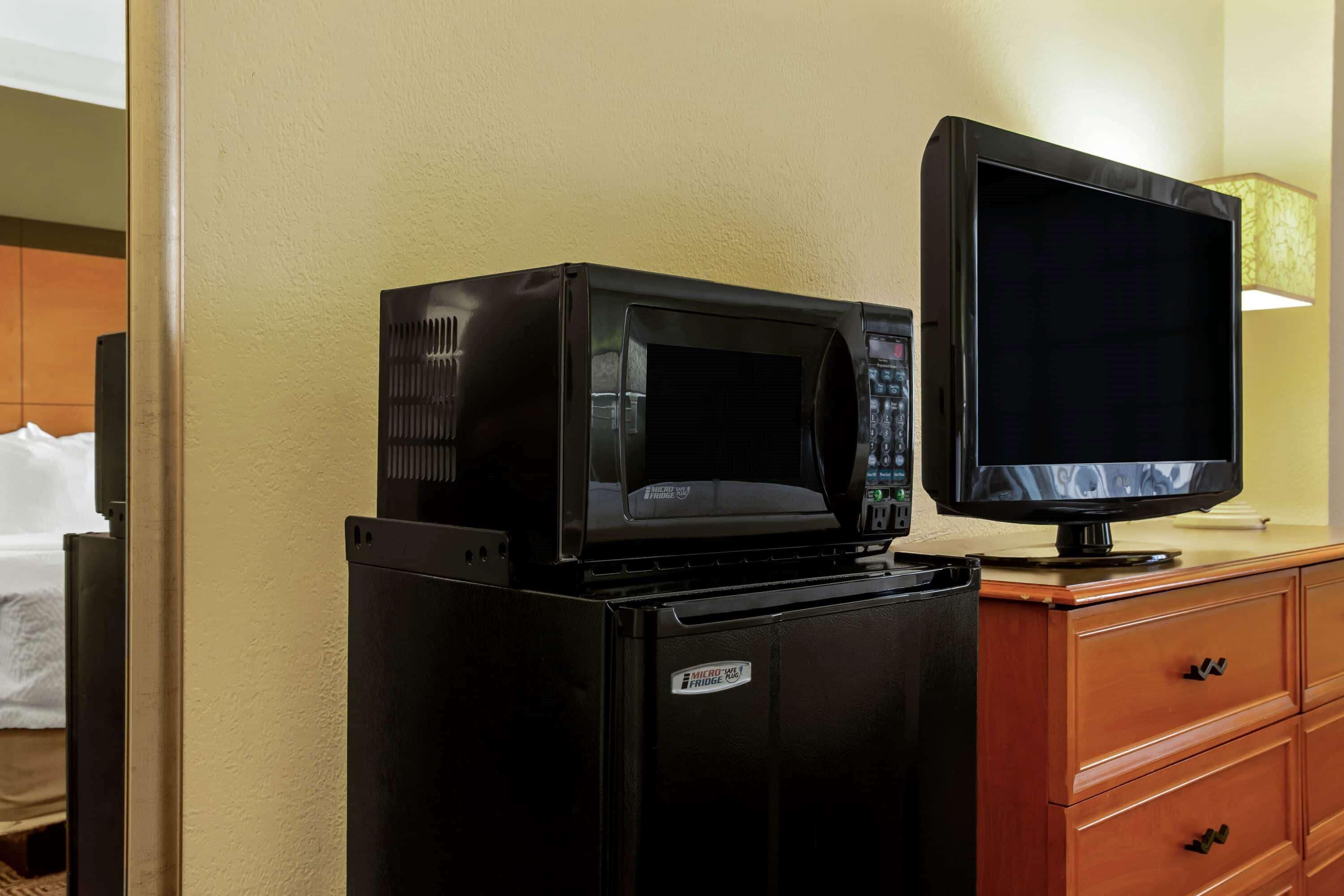 A compact kitchenette with a microwave and a television on a wooden cabinet.