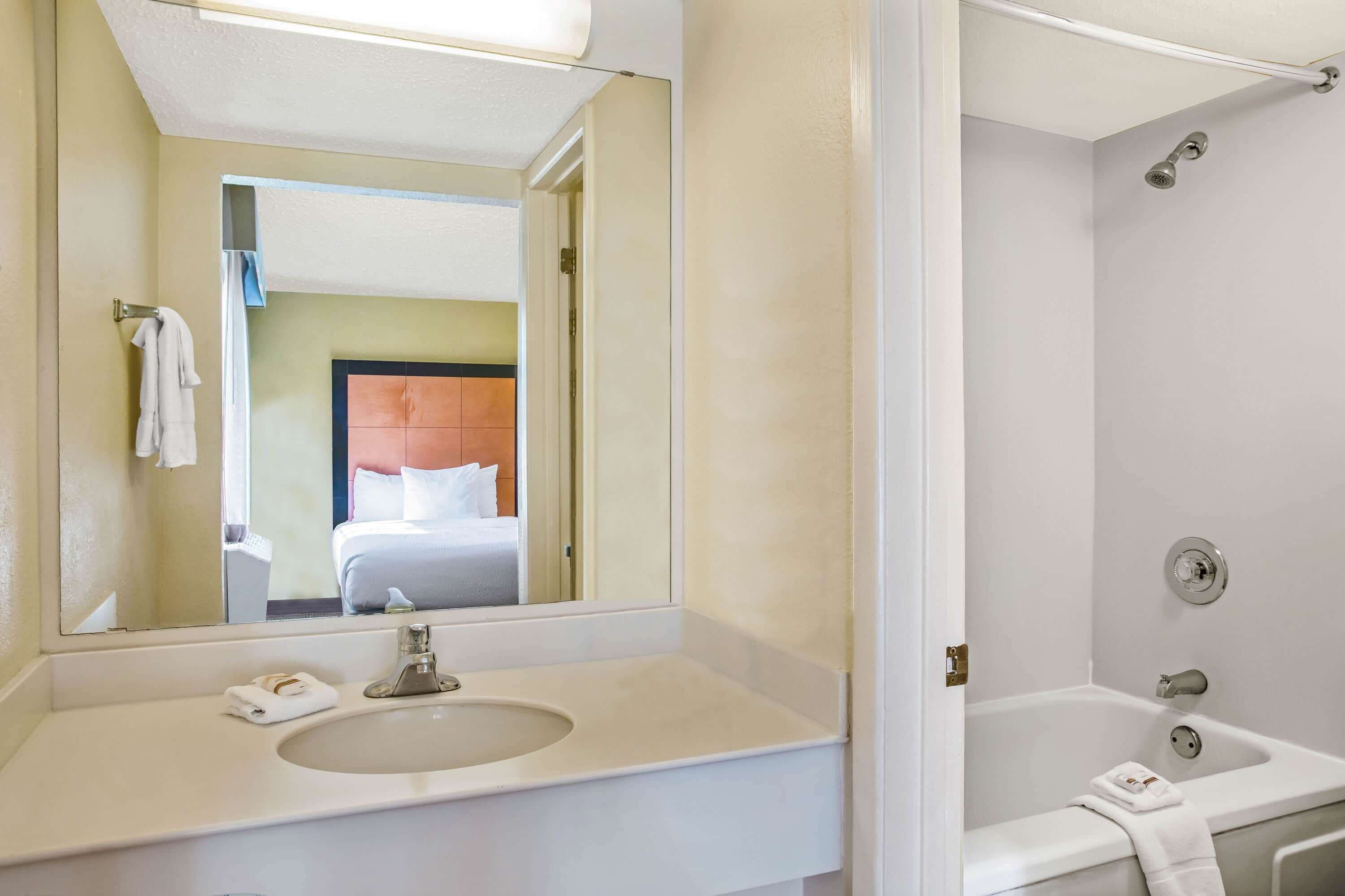 A hotel bathroom with a large mirror, a sink, and a bathtub.