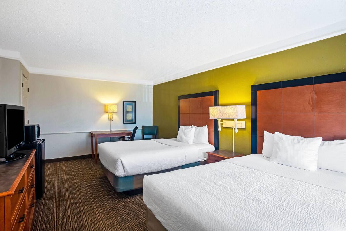 A hotel room with two beds, a desk with a TV, and a chair.