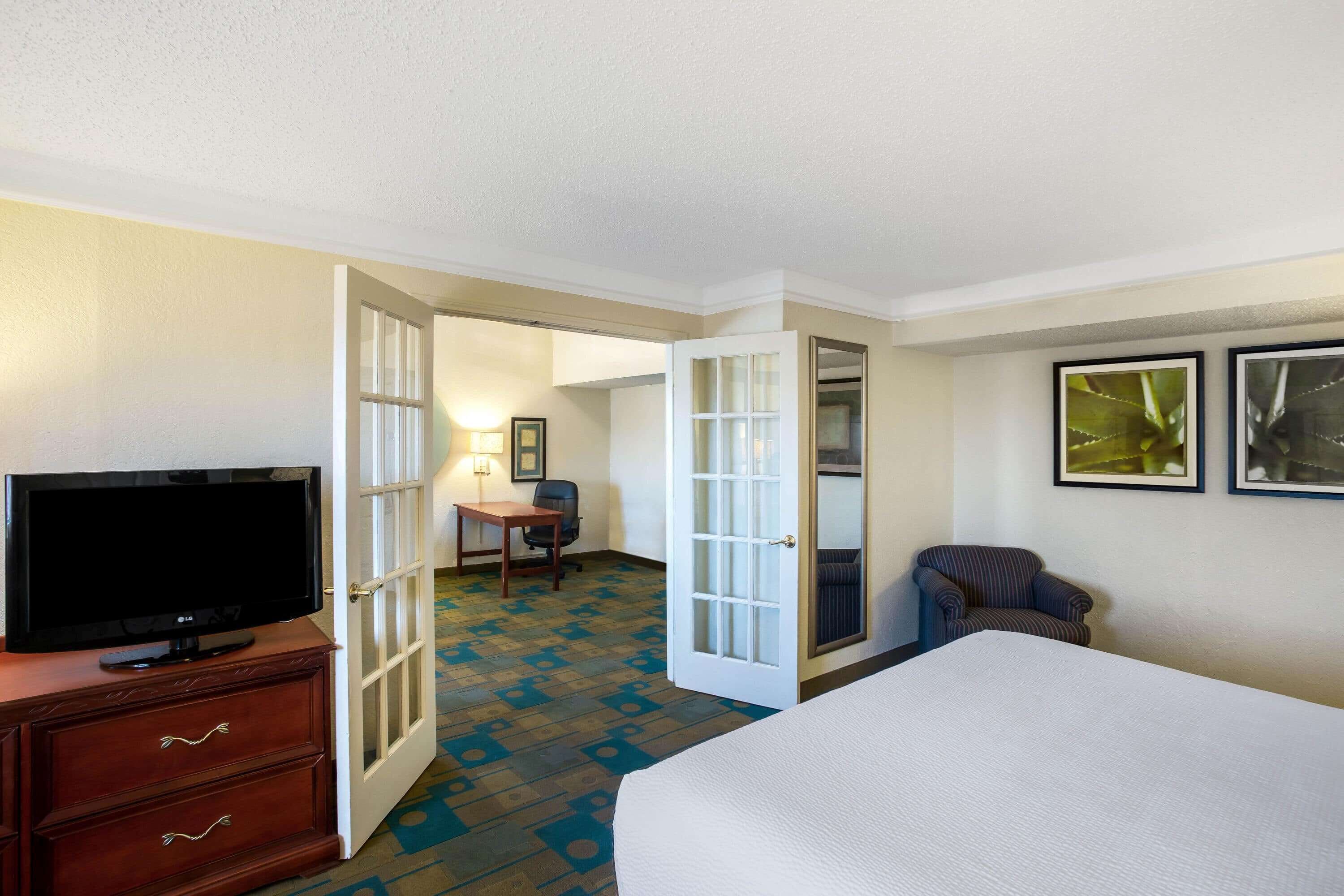 A hotel room with a bed, a TV on a dresser, a desk with a chair, and two framed pictures on the wall.