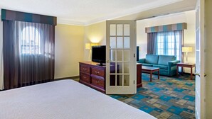 Een hotelkamer met een bed, een televisie op een dressoir, een bank en een deur naar een andere kamer.