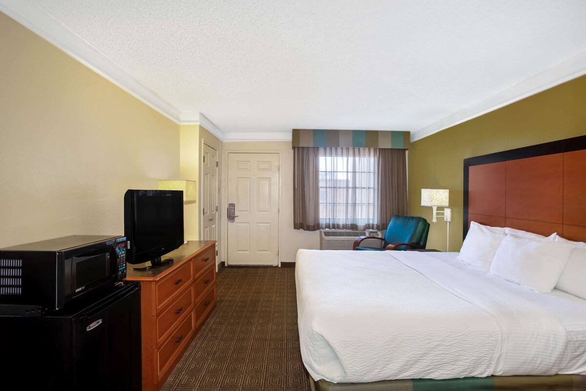 A hotel room with a bed, a television, a dresser, a chair, and a window with curtains.