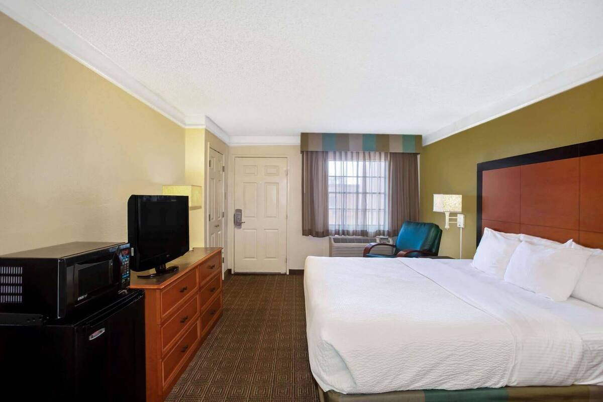 A hotel room with a bed, a television on a dresser, a chair, and a door.