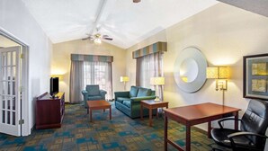 Een hotelkamer met een plafondventilator, een bank, een stoel, een bijzettafeltje en een televisie op een houten standaard.