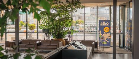 En modern inredning med sittplatser, en stor växt och utsikt över staden genom stora fönster.