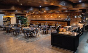 A restaurant with wooden flooring, multiple tables and chairs, a central bar area, and a large mural on the back wall.