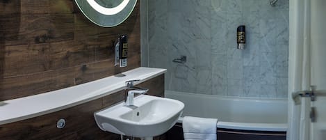 Une salle de bain moderne avec un meuble-lavabo en bois, un lavabo blanc, un miroir rond avec éclairage intégré, une douche avec un mur en marbre et une baignoire.