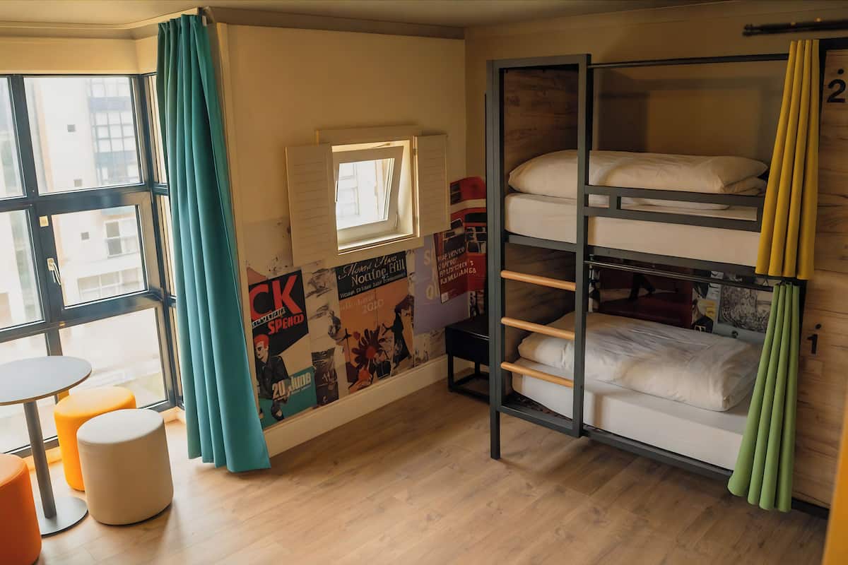 A bunk bed room with a window, a small table, and a poster on the wall.