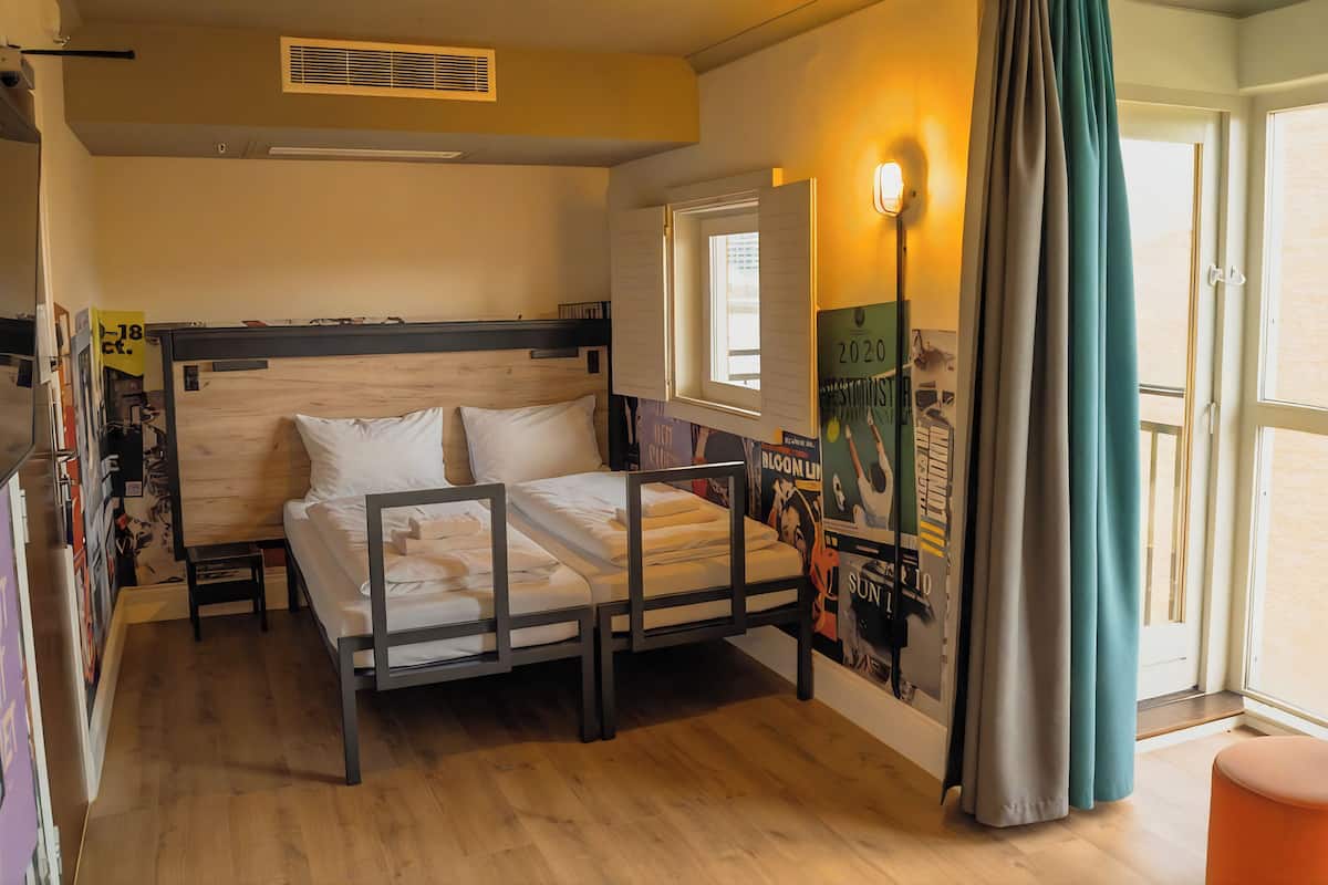 A bedroom with a wooden bed, a window, a door, and a poster on the wall.