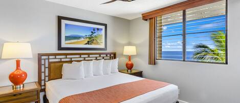 A hotel room with a bed, two bedside tables, a ceiling fan, a window with blinds, and a framed picture on the wall.