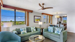 A living room with two green sofas, a glass coffee table, and a ceiling fan. - Maui Beach Vacation Club (Kihei)