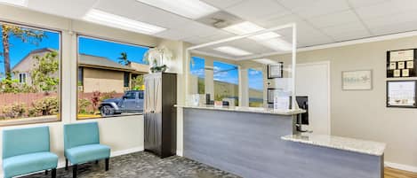 A reception area with a counter, two chairs, a refrigerator, and a view of a parked truck outside.