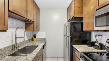 A kitchen with wooden cabinets, a stainless steel sink, a black refrigerator, and a microwave.