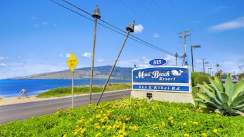 Une enseigne pour le Maui Beach Resort, avec une vue sur la plage, une enseigne jaune indiquant « Drifting Sand » et un ciel bleu clair.