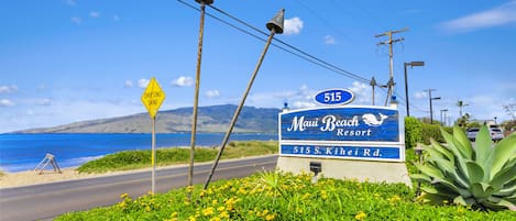 A sign for Maui Beach Resort with a beach view, a yellow 'Drifting Sand' sign, and a clear blue sky.