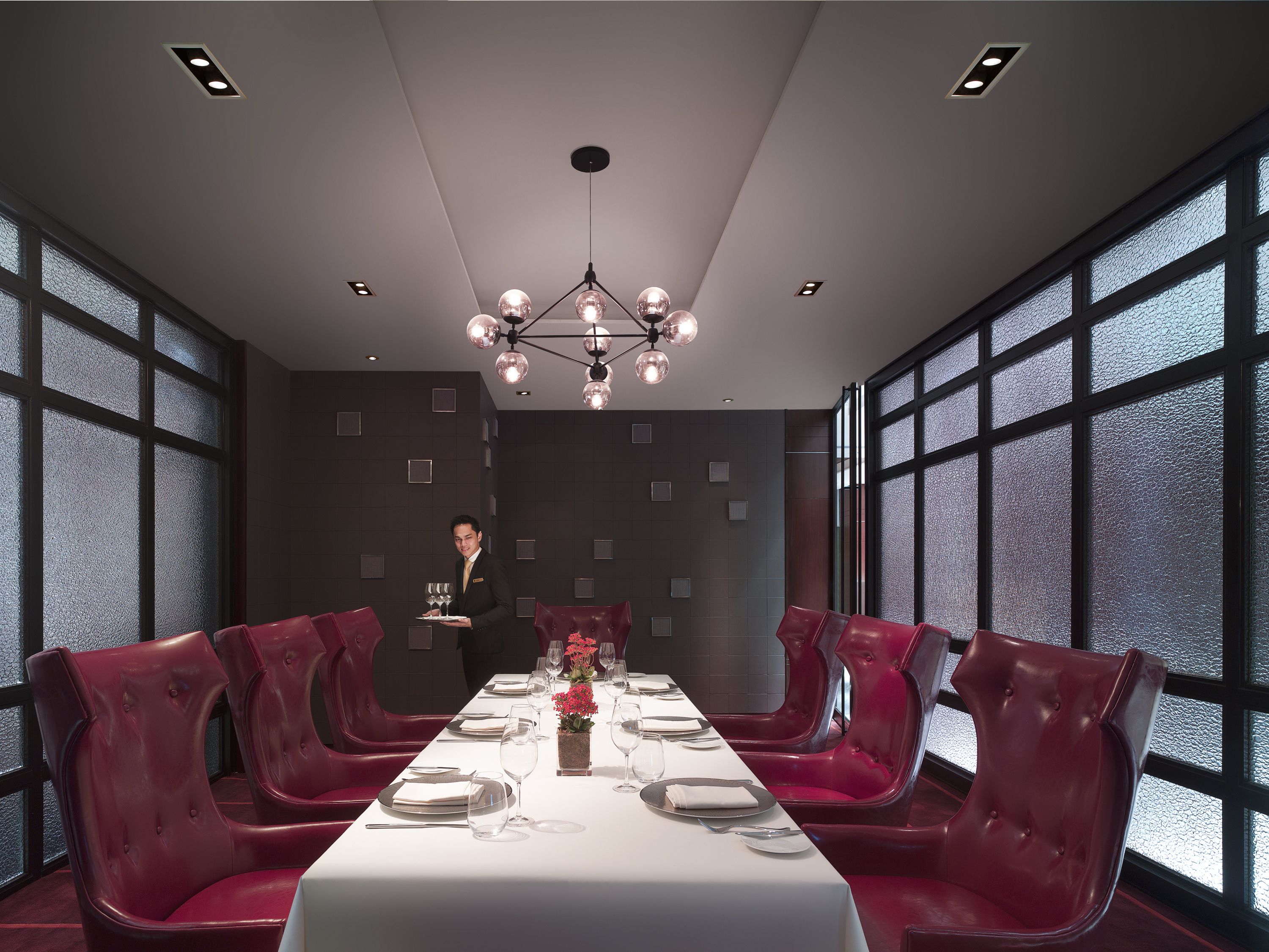 A dining room with a long table set for a meal, surrounded by red upholstered chairs.