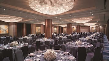 A banquet hall with round tables set for dining, large chandeliers, and artwork on the walls.