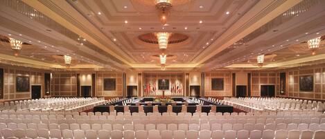 A large conference room with rows of white chairs, a long table, and a chandelier.