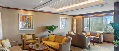 A modern hotel lobby with a sofa, armchairs, a coffee table, and a large window offering a city view.