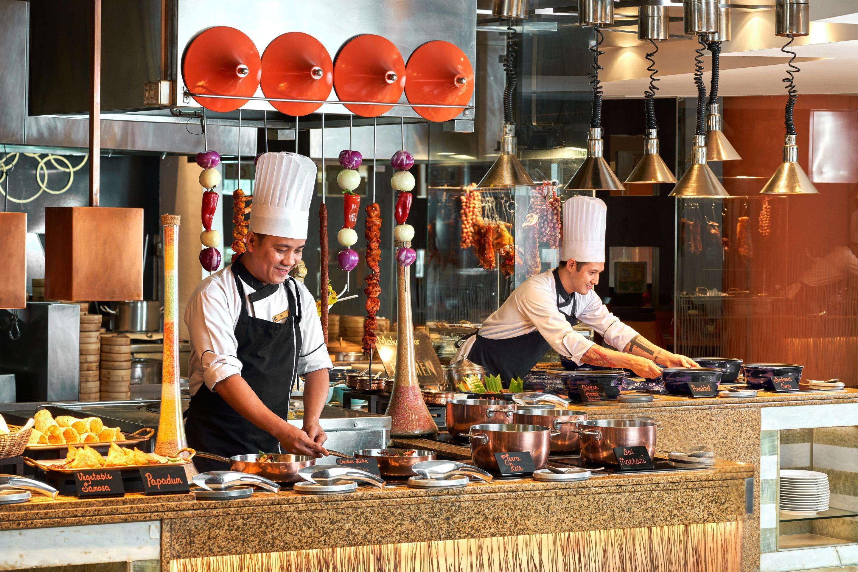 A kitchen with chefs preparing food, various cooking utensils, and ingredients on the counter.