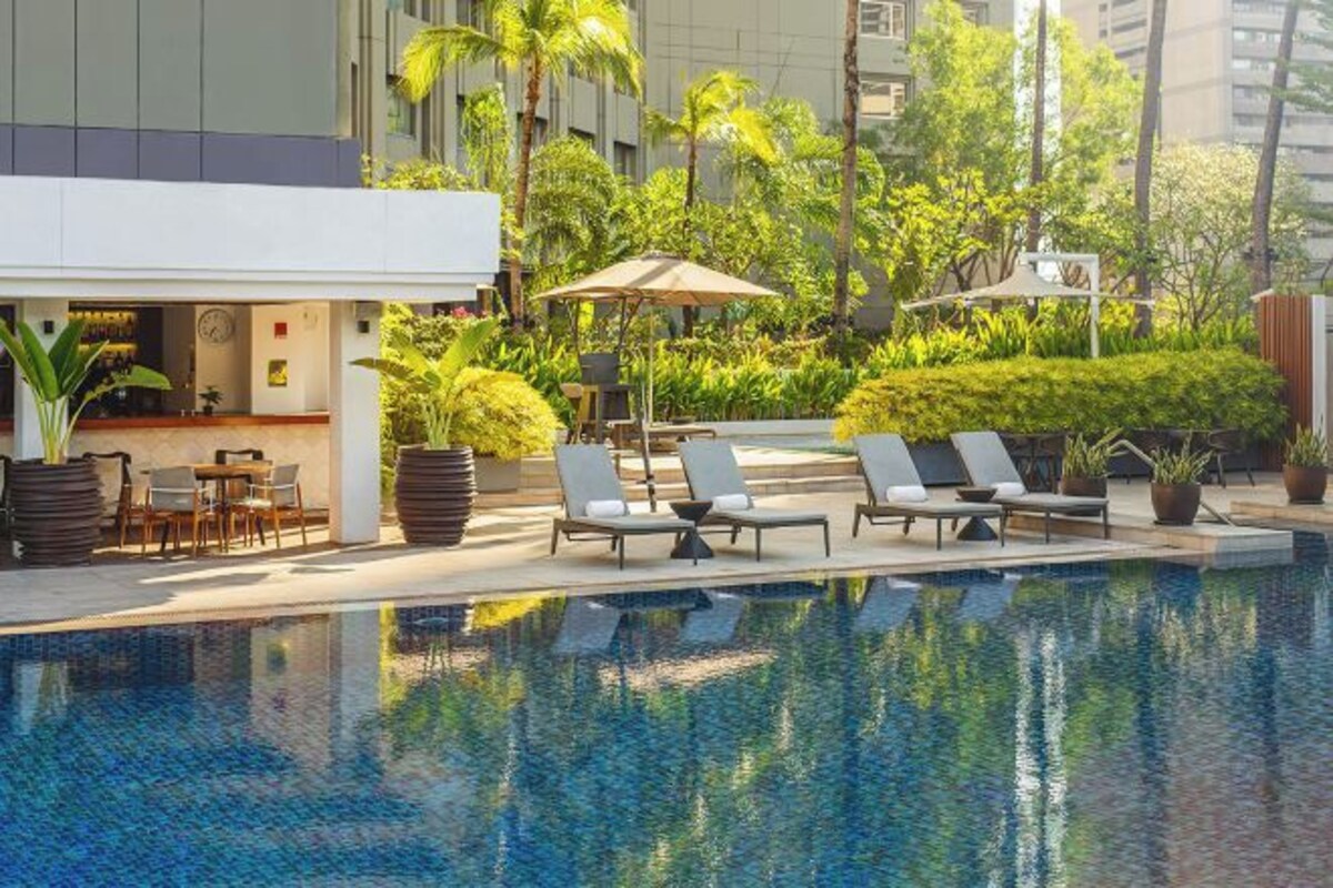 A pool area with lounge chairs and a bar, surrounded by greenery and palm trees.