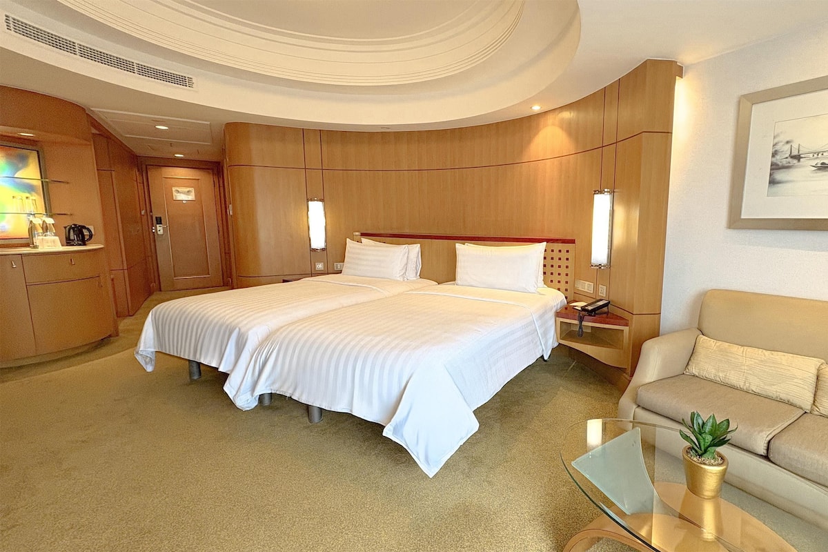 A hotel room with a large bed, a sofa, a coffee table, a nightstand, and a painting on the wall.