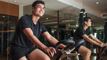 Two individuals on stationary bikes in a gym with glass walls and a punching bag in the background.