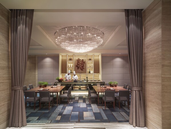 A modern dining area with a central island, two chefs, and a chandelier.