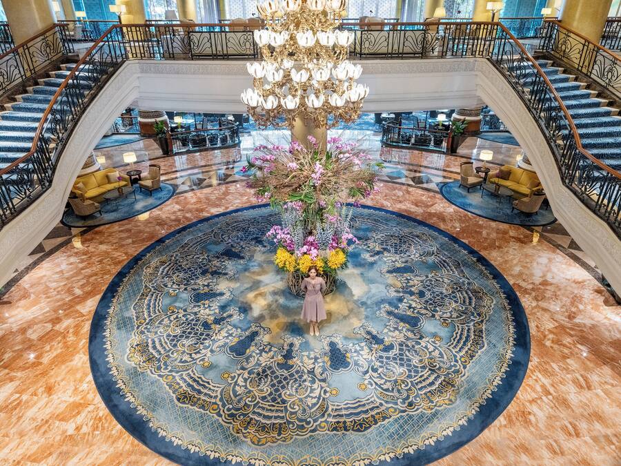 A grand lobby with a central floral arrangement, a chandelier, and a circular patterned carpet.
