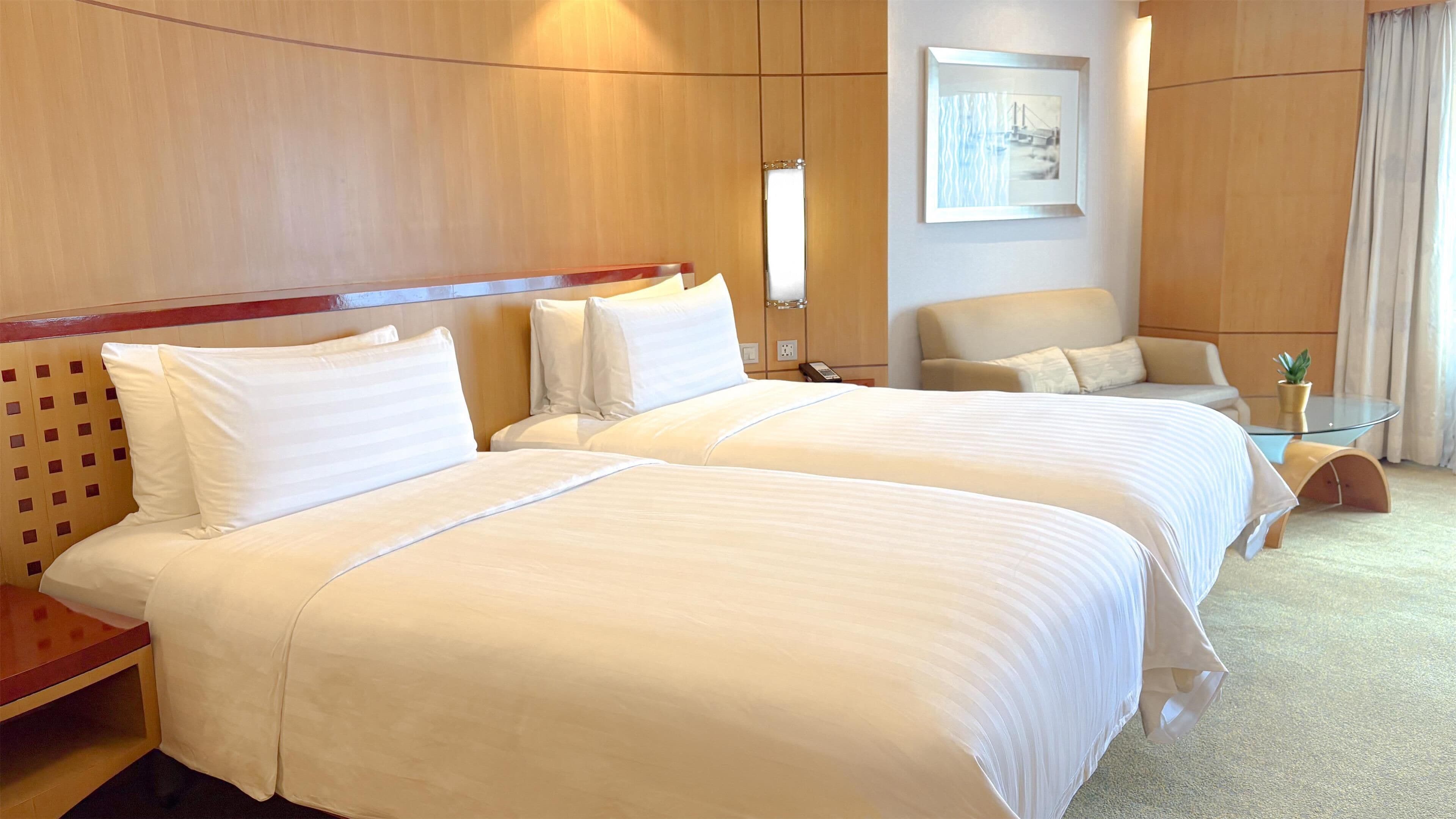 A hotel room with two beds, a small table, a chair, and a painting on the wall.