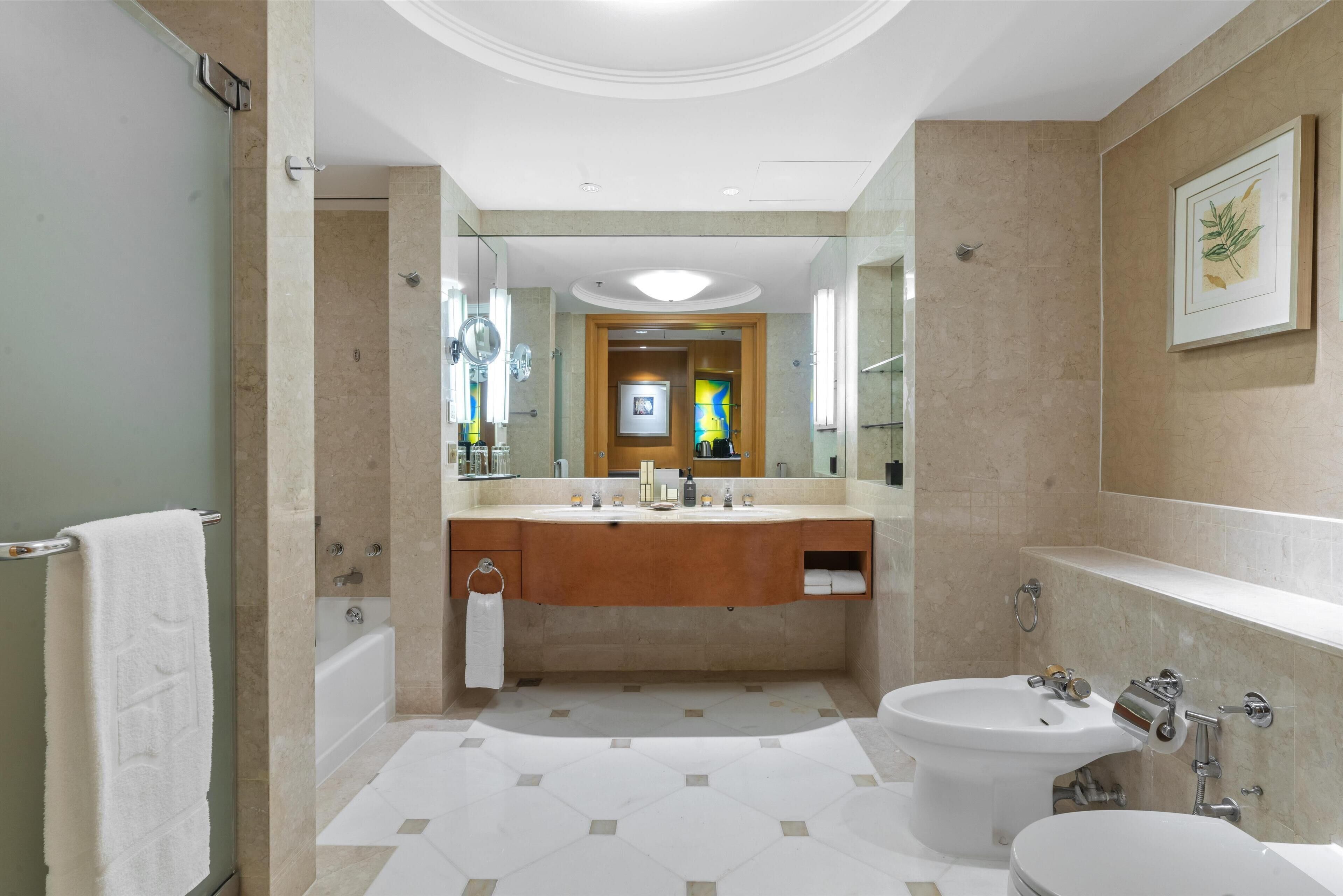 A modern bathroom with a large mirror, a bathtub, a sink, and a bidet.