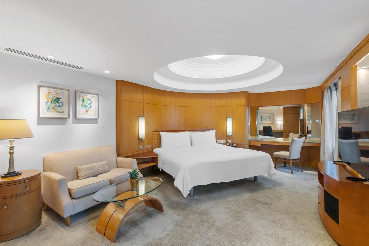 A hotel room with a bed, a sofa, a glass coffee table, a desk, and a mirror.