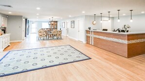 A spacious hotel lobby with a reception desk, a dining area with chairs, and a patterned rug on the floor.