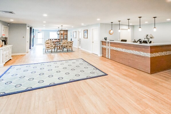 Un hall d’hôtel spacieux avec un comptoir d’accueil, un espace repas avec des chaises et un tapis à motifs sur le sol.