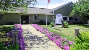 A building with a flag, a sign, and a pathway lined with flowers.