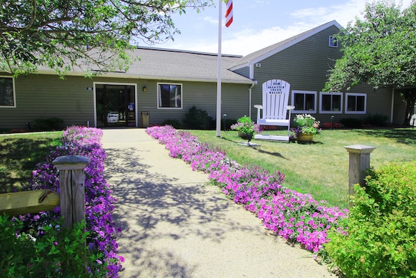 A building with a flag, a sign, and a pathway lined with flowers. - Brewster Green Resort (Brewster)