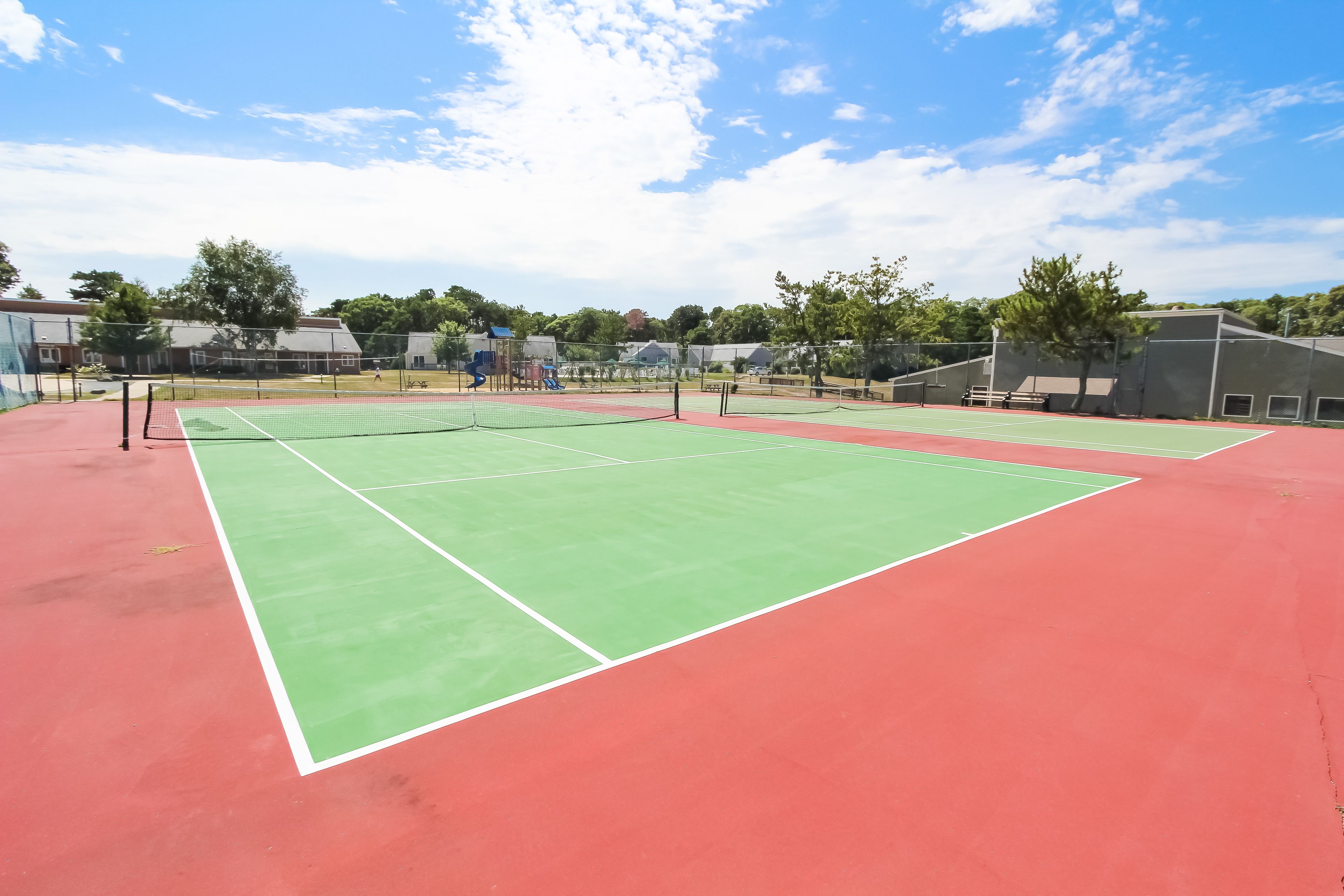 Un court de tennis avec un filet au milieu, entouré d’une surface de jeu rouge et verte.