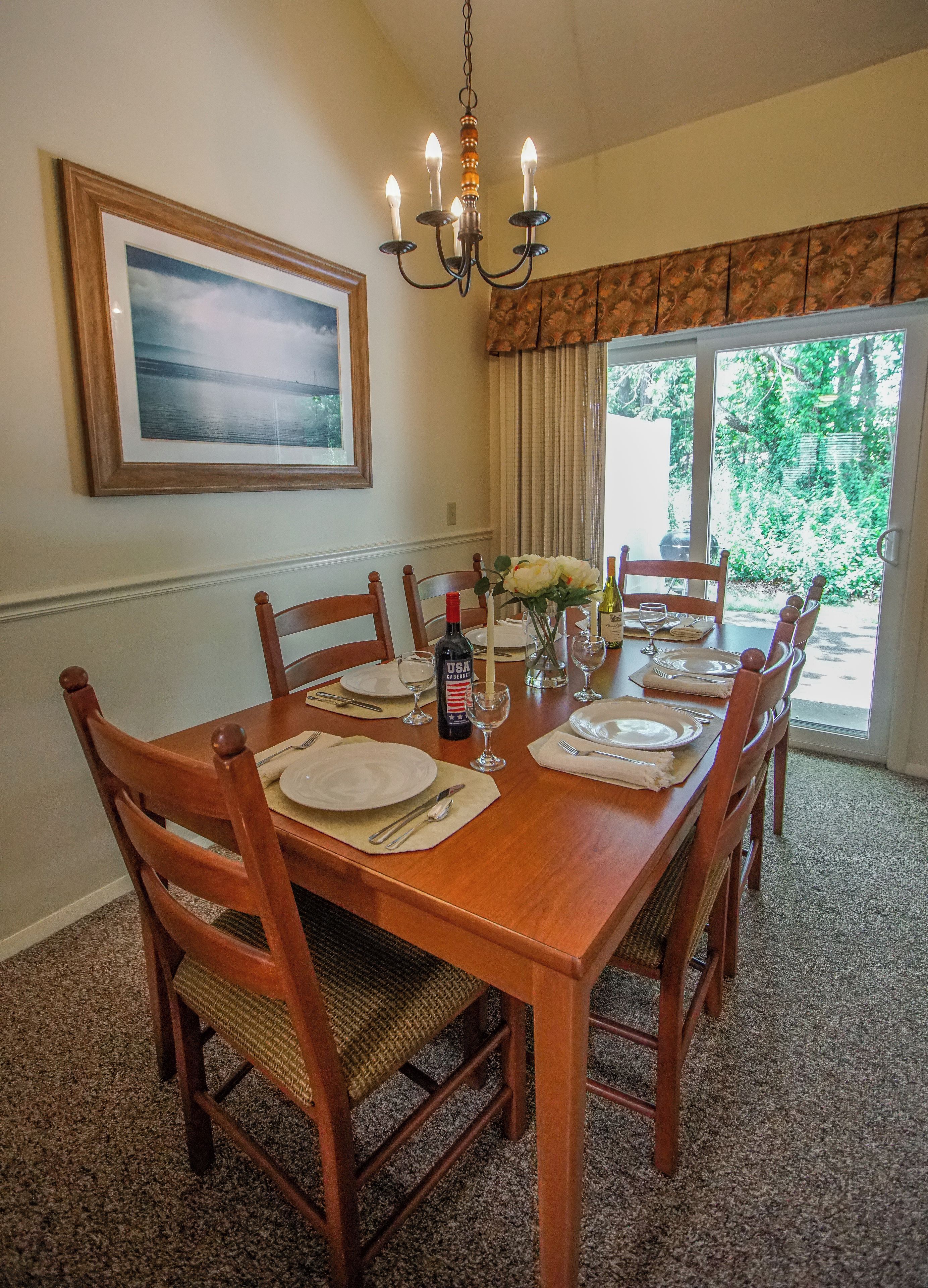 A dining room with a wooden table set for six, surrounded by chairs, a chandelier, and a framed picture on the wall.