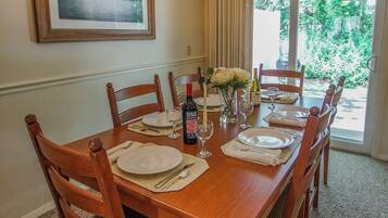 A dining room with a wooden table set for six, surrounded by chairs, a chandelier, and a framed picture on the wall.