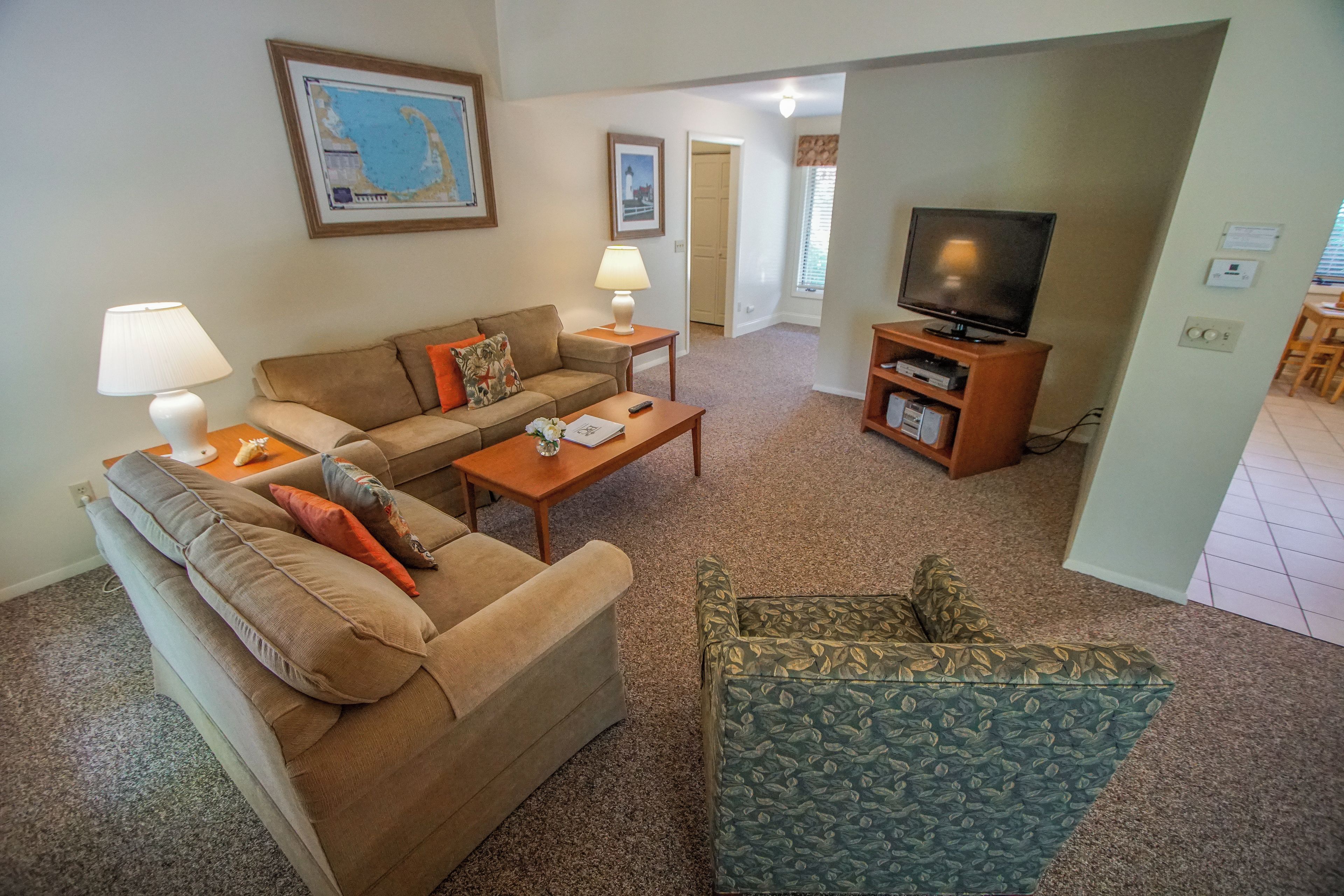 A living room with a sofa, a coffee table, a TV stand, and a patterned armchair.