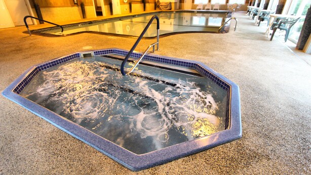 A hot tub with a tiled edge and a metal ladder, surrounded by a carpeted floor and wooden walls.