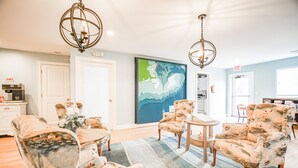 A spacious living room with a large abstract painting, two chandeliers, and a coffee machine.