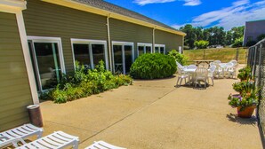 A patio area with white lounge chairs, a building with large windows, and a clear blue sky.