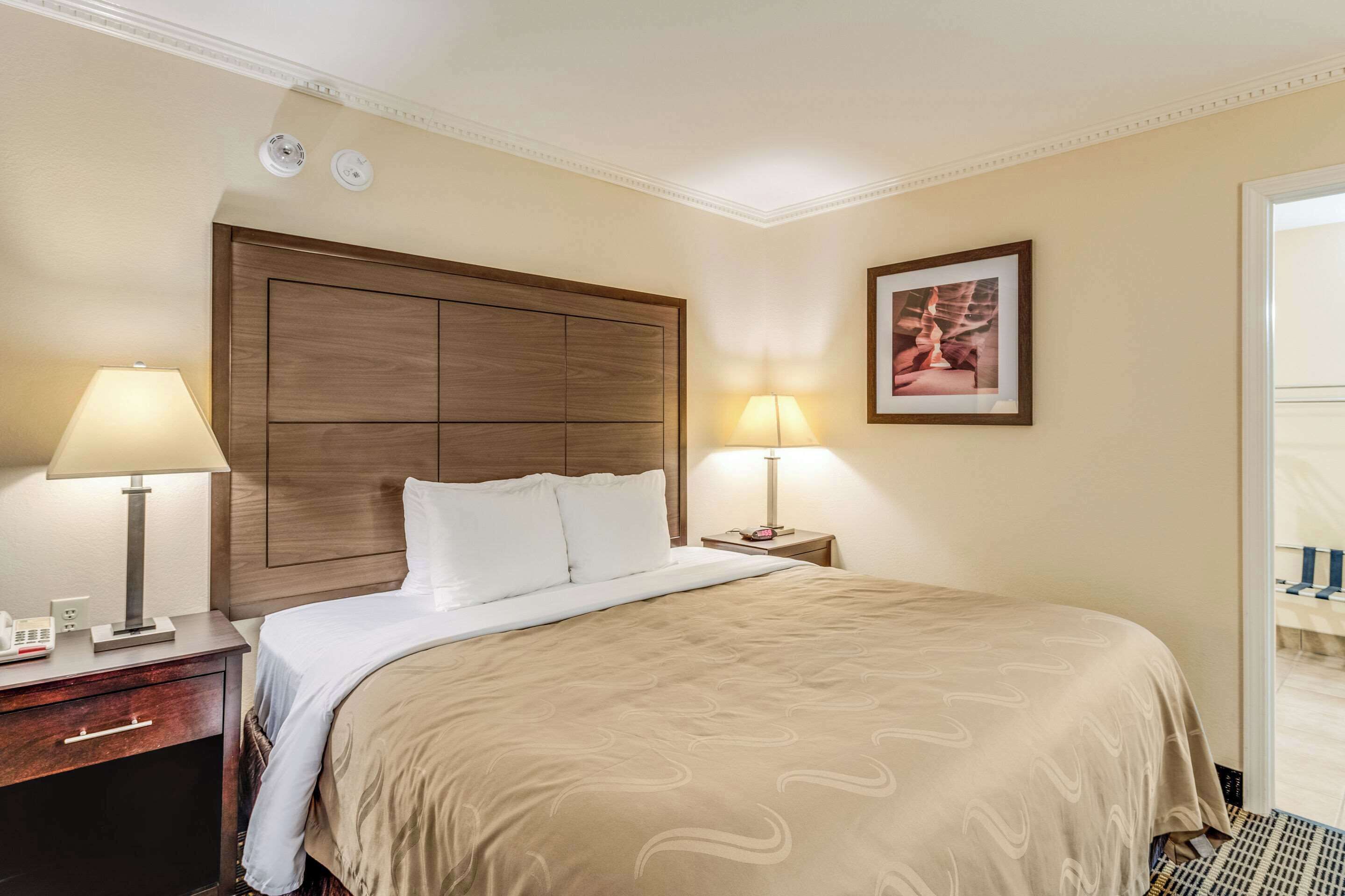 A hotel room with a large bed, two bedside lamps, a nightstand, and a framed picture on the wall.