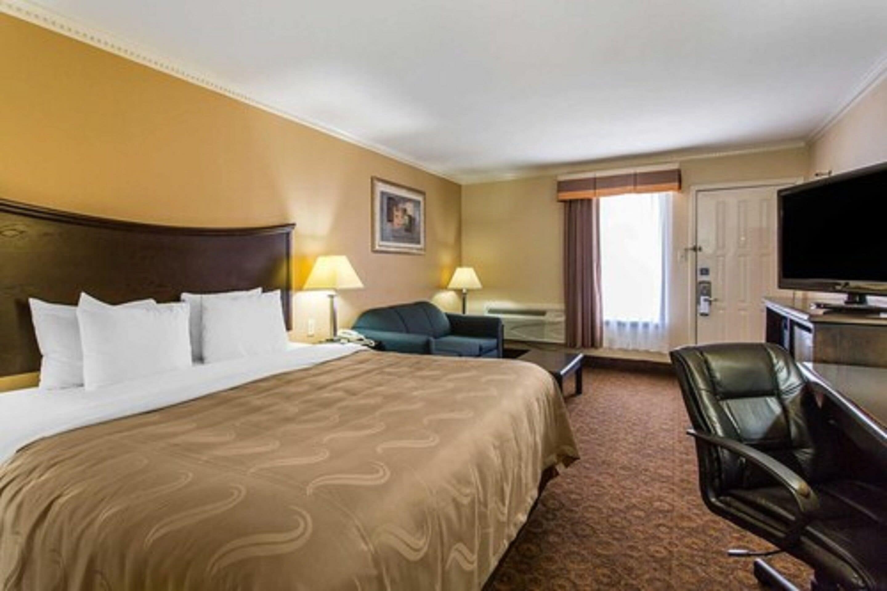 Une chambre d’hôtel avec un grand lit, un bureau avec une chaise, une télévision et une fenêtre avec des rideaux.