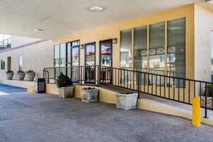 Entrada de un hotel con una galería techada, ventanas amplias y fachada amarilla.