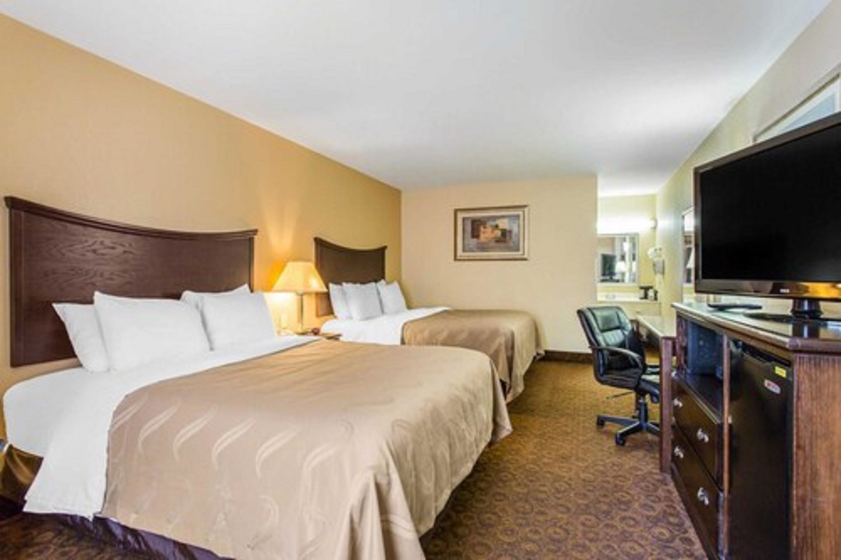 A hotel room with two beds, a desk, a chair, a television, and a framed picture on the wall.