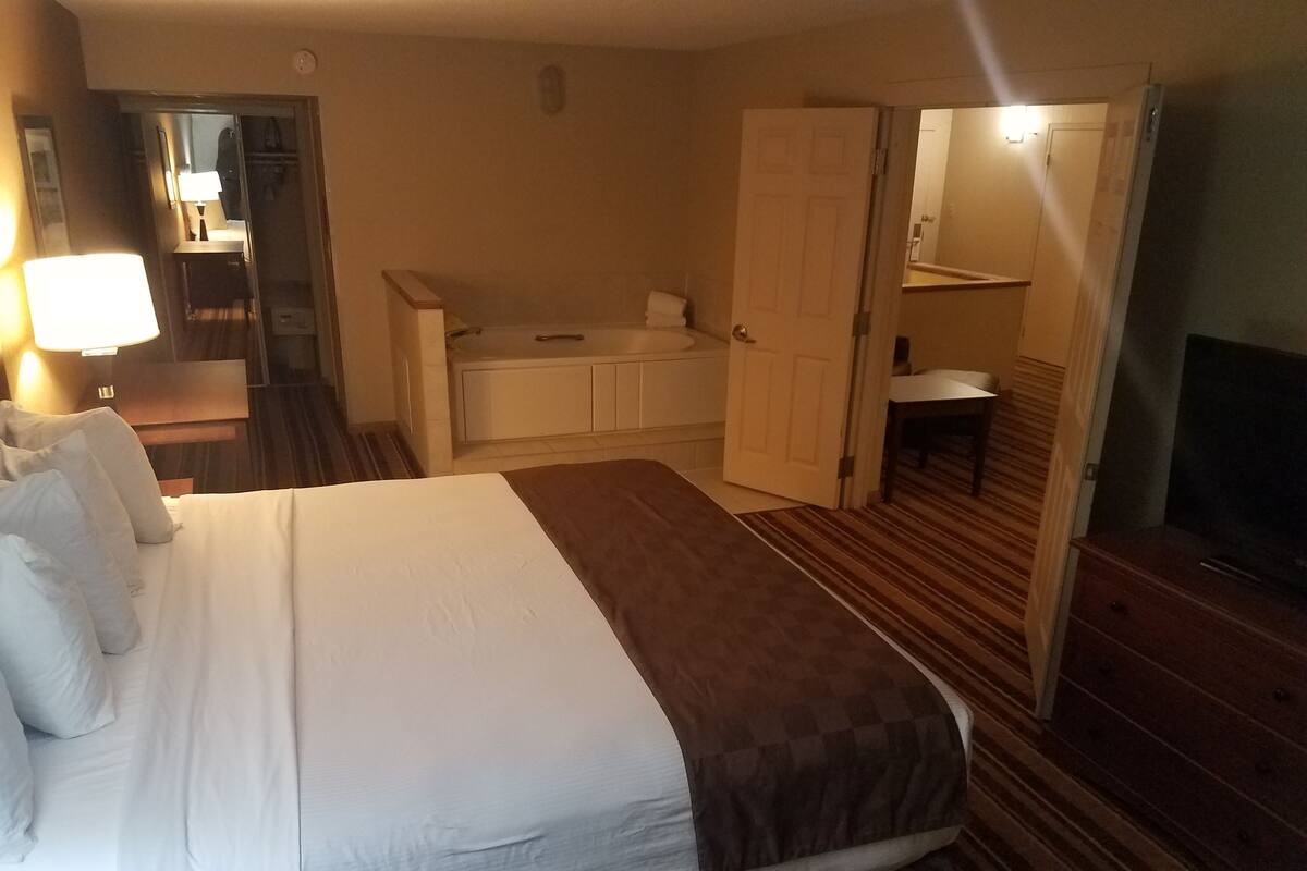A hotel room with a large bed, a desk with a lamp, a bathroom, and a TV.